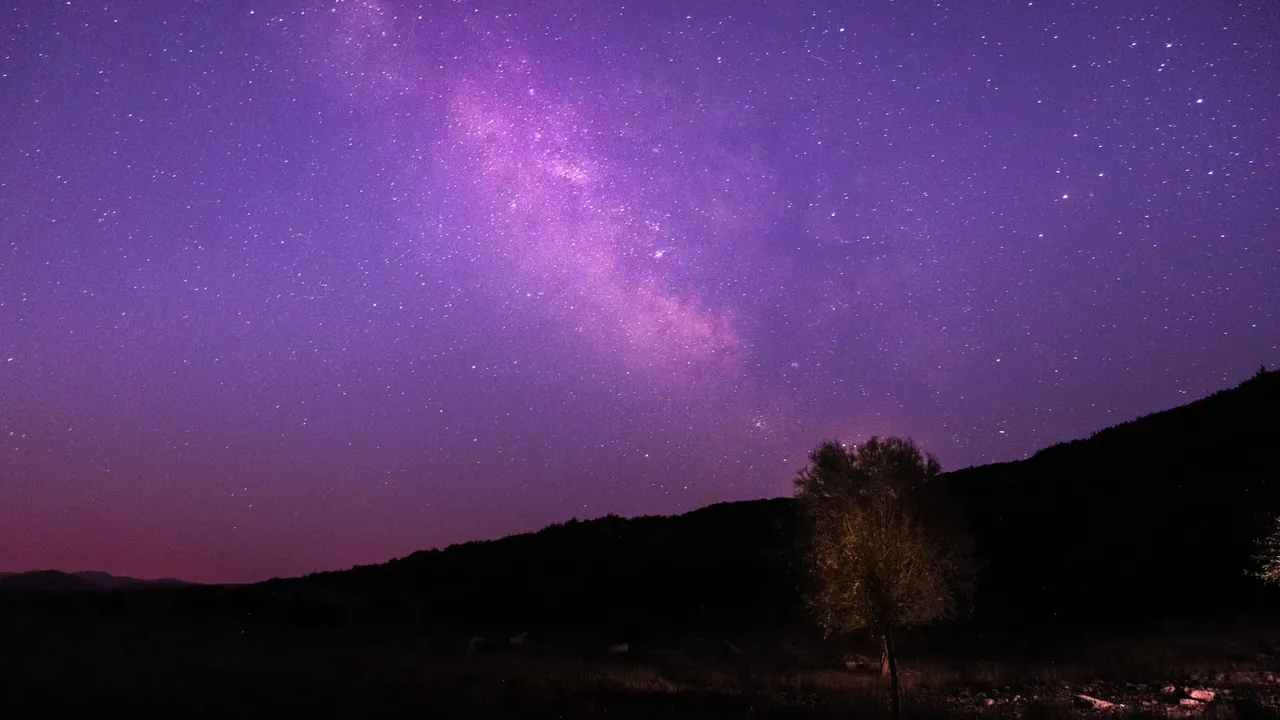 A starry purple night sky over distant hills